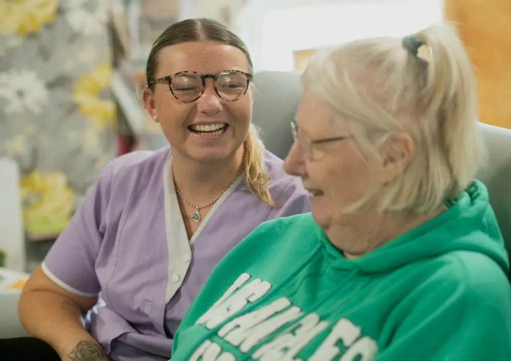 A support worker and an older woman share a laugh.