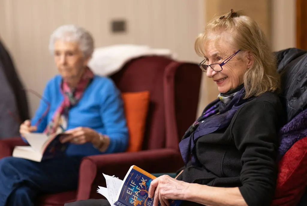 Two women sit in armchairs, each reading, and talk about their books.